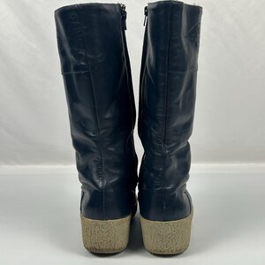 May include: A pair of navy blue leather boots with a beige sole. The boots have a zipper on the side and a textured pattern near the top. The boots are approximately 12 inches tall.