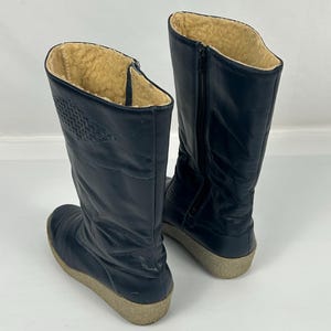 May include: A pair of navy blue winter boots. The boots have a tall shaft with a zipper on the side and a textured design on the upper. The interior is lined with a tan, fuzzy material. The soles are a light beige color.
