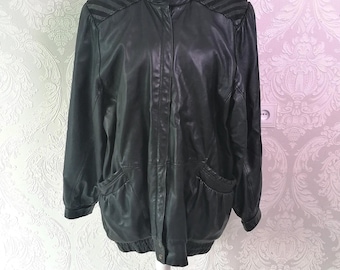 May include: A black leather jacket featuring a high collar, a front button closure, and ribbed detailing on the shoulders. The jacket includes two front pockets with gathered edges and a ribbed hemline, providing a structured and classic silhouette.