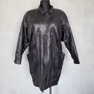 May include: A long black leather jacket with a button-up front and a collar. The jacket has a relaxed fit and features two large pockets on the front.
