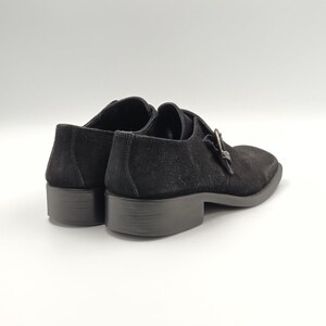 K&ouml;nnte beinhalten: Ein Paar schwarze Schnallenschuhe aus Wildleder. Die Schuhe haben ein klassisches Design mit einer spitzen Zehenpartie und einem niedrigen Absatz.