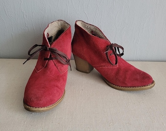 May include: A pair of red suede ankle boots with lace-up closures and a low block heel.
