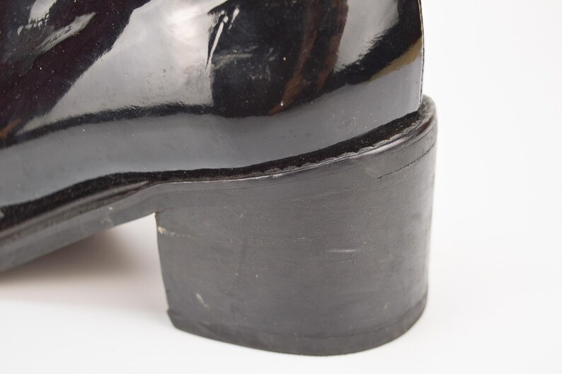 Puede incluir: Bota de tac&oacute;n de charol negro con una suela gruesa de goma negra.