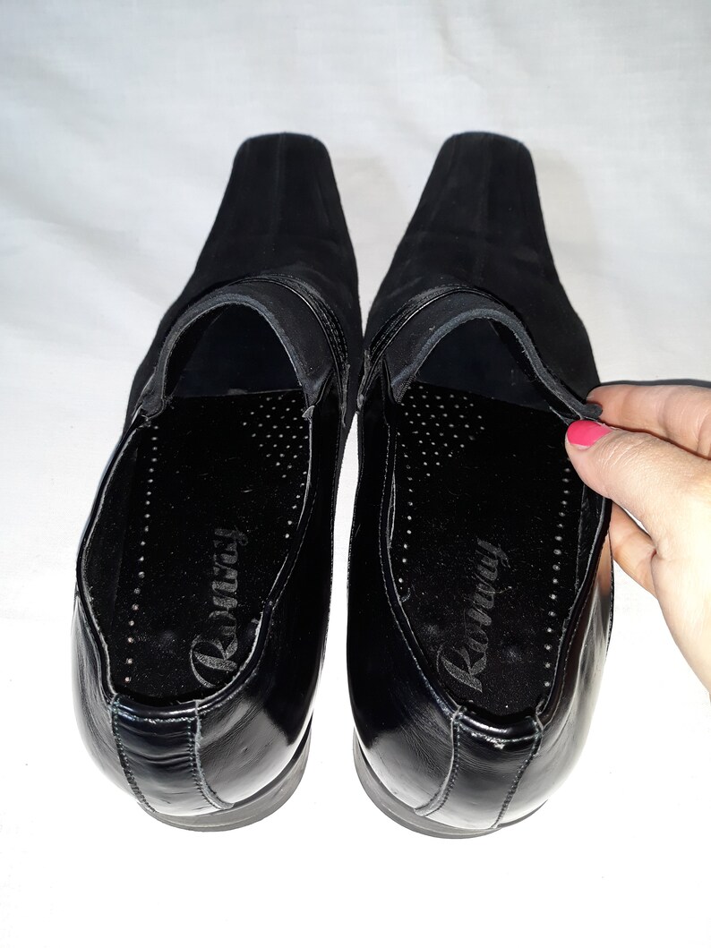Puede incluir: Un par de zapatos negros de cuero con un empeine de ante negro. Los zapatos tienen una suela de cuero negro y una plantilla de cuero negro. La plantilla est&aacute; etiquetada como "Runway".