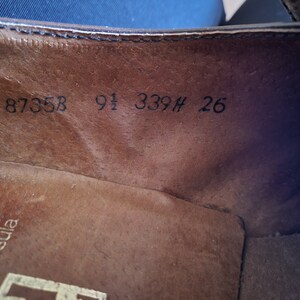 May include: Close-up of the inside of a brown leather shoe with the numbers 8735B 9 1/2 339H 26 printed on the insole.