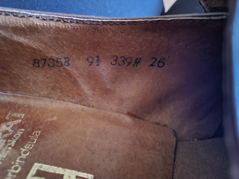 May include: Close-up of the inside of a brown leather shoe with the numbers 8735B 9 1/2 339H 26 printed on the insole.