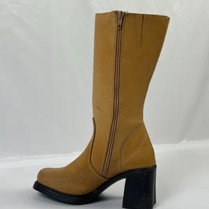 Puede incluir: Bota alta hasta la rodilla de cuero color canela con tac&oacute;n de bloque negro. La bota tiene una cremallera lateral y una puntera cuadrada. El tac&oacute;n mide aproximadamente 7,6 cm.