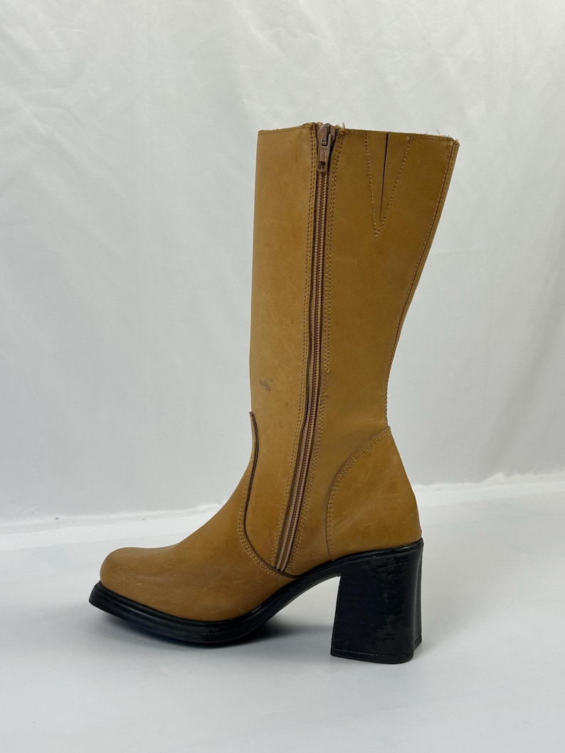 Puede incluir: Bota alta hasta la rodilla de cuero color canela con tac&oacute;n de bloque negro. La bota tiene una cremallera lateral y una puntera cuadrada. El tac&oacute;n mide aproximadamente 7,6 cm.
