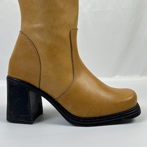 Puede incluir: Bota alta de cuero color canela con punta cuadrada y tac&oacute;n de bloque negro. La bota tiene una ca&ntilde;a redondeada y una suela negra. El tac&oacute;n mide aproximadamente 7.6 cm.