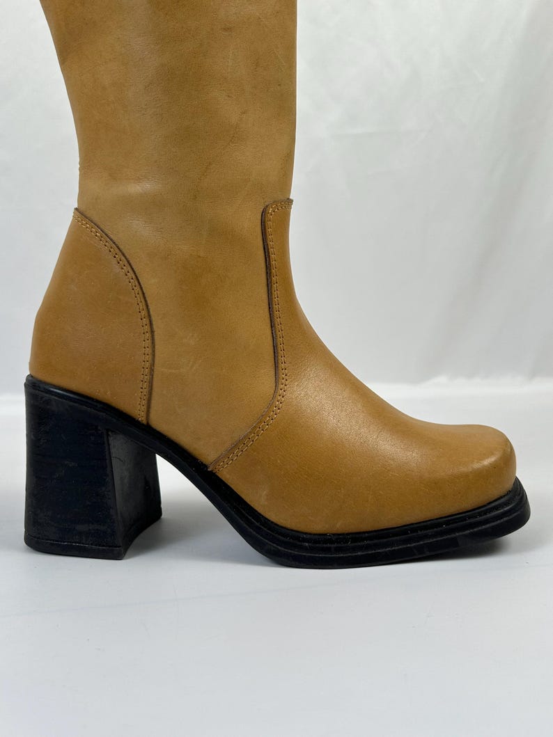 Puede incluir: Bota alta de cuero color canela con punta cuadrada y tac&oacute;n de bloque negro. La bota tiene una ca&ntilde;a redondeada y una suela negra. El tac&oacute;n mide aproximadamente 7.6 cm.