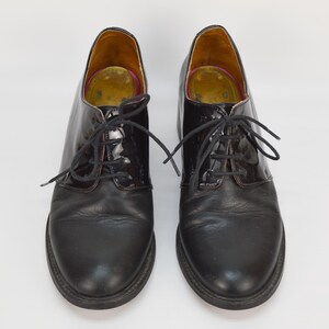 Puede incluir: Un par de zapatos negros de cuero con cordones y puntera de charol. Los zapatos tienen un estilo oxford cl&aacute;sico.