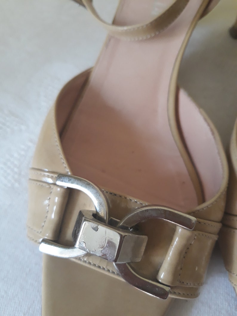 May include: Beige leather heeled sandals with a silver buckle detail.