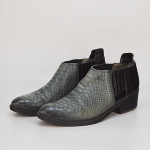 Peut inclure: Une paire de bottines grises et noires à motif peau de serpent. Les bottines ont un talon bas et une pointe pointue.