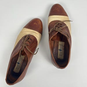 May include: A pair of brown and tan oxford shoes with a woven fabric panel. The shoes have brown laces and the brand name "King Street" is visible inside the shoe.