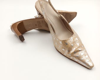 Puede incluir: Un par de tacones de slingback dorados con un patrón de lunares plateados. Los tacones son de cuero y tienen una punta puntiaguda. Los zapatos son talla 39.