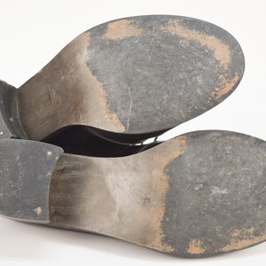 Puede incluir: Primer plano de las suelas de un par de zapatos de cuero negro. Los zapatos tienen una parte superior de cuero liso y una suela de goma.