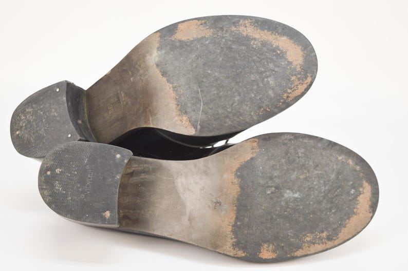 Puede incluir: Primer plano de las suelas de un par de zapatos de cuero negro. Los zapatos tienen una parte superior de cuero liso y una suela de goma.