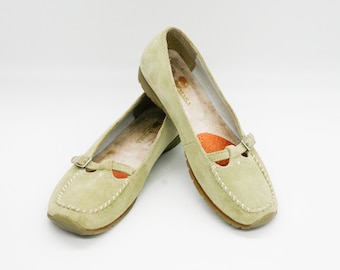 May include: A pair of light green suede shoes with a buckle fastening. The shoes have a round toe and a low heel.