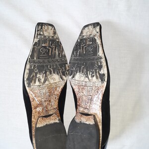 Puede incluir: Un par de zapatos de ante negro con puntera cuadrada y un patr&oacute;n decorativo en la suela. Los zapatos son talla 40.
