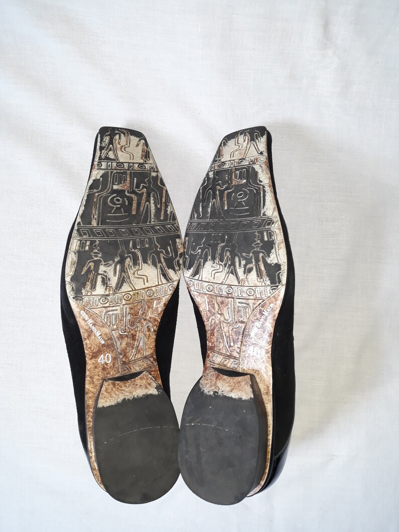 Puede incluir: Un par de zapatos de ante negro con puntera cuadrada y un patr&oacute;n decorativo en la suela. Los zapatos son talla 40.