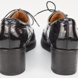 Puede incluir: Par de zapatos de tac&oacute;n de charol negro con cierre de cordones. Los zapatos tienen un tac&oacute;n grueso y una puntera redonda.