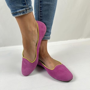 May include: A pair of bright pink suede ballet flats featuring a rounded toe and a contrasting neon yellow trim along the collar. The shoes have a low-cut silhouette and a flat sole, providing a simple and clean design for everyday footwear.