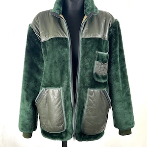 May include: A dark green jacket with a faux fur body and olive green leather panels. The jacket has a zip-up front, two front pockets, and a collared neckline. The cuffs and collar are a darker shade of green.