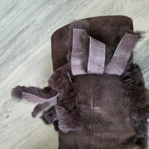 May include: Brown suede boots with a faux fur trim and brown suede ties. The boots have a decorative bow on the top.