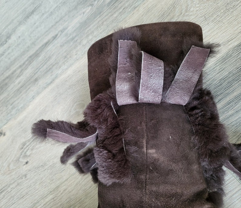 May include: Brown suede boots with a faux fur trim and brown suede ties. The boots have a decorative bow on the top.