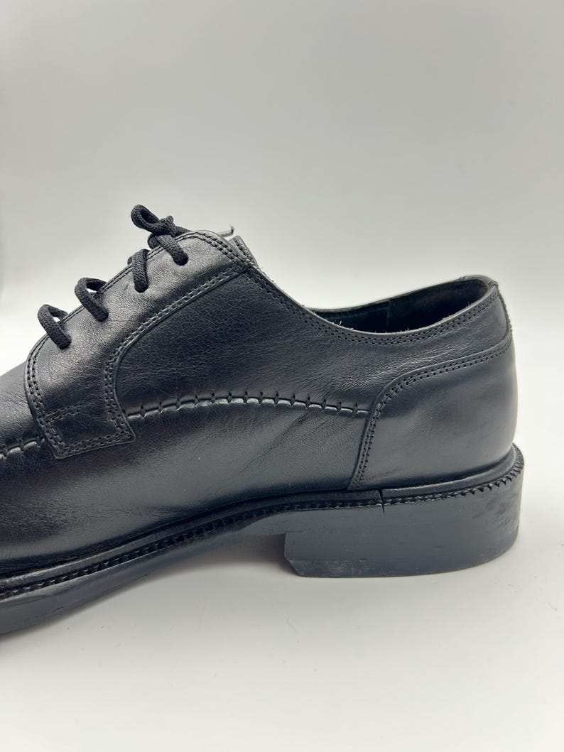 K&ouml;nnte beinhalten: Schwarzer Lederschuh mit Schn&uuml;rverschluss. Der Schuh hat ein gen&auml;htes Design entlang der N&auml;hte und einen niedrigen Absatz. Geeignet f&uuml;r formelle Anl&auml;sse.