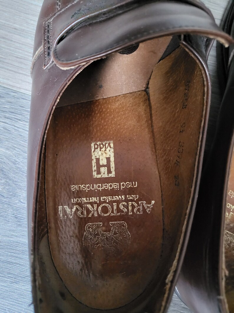 May include: Close-up of the inside of a brown leather shoe with the text "ARISTOKRAT den Svenska hertskon med laderinnersula" printed on the insole.