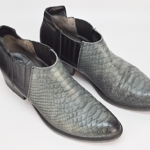 May include: A pair of black and gray ankle boots with a snakeskin pattern. The boots have a pointed toe and a low heel.