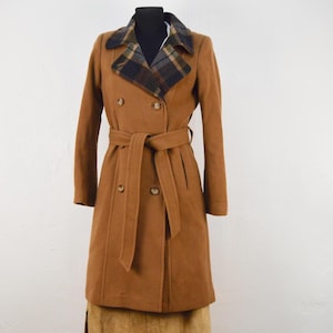 Puede incluir: Un abrigo marrón de doble botonadura con cuello de cuadros y cinturón a juego.
