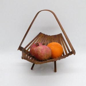 May include: A brown wooden fruit basket with a handle, holding a red pomegranate and an orange.