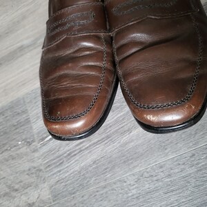 May include: A pair of brown leather loafers with a stitched edge. The loafers have a slightly worn look.