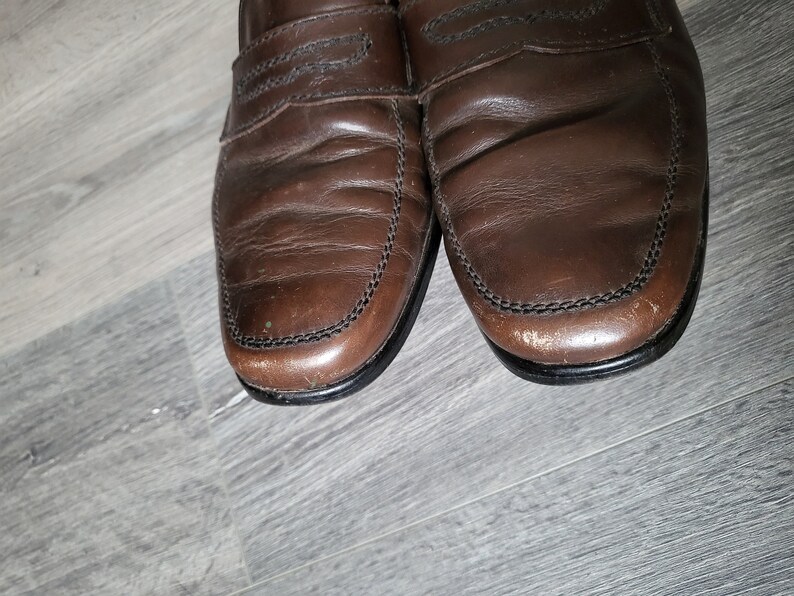 May include: A pair of brown leather loafers with a stitched edge. The loafers have a slightly worn look.