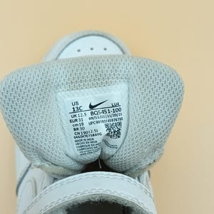 以下が含まれることがあります： 白いベルクロストラップが付いた白い子供用スニーカー。サイズタグには、US 13C、UK 12.5、EUR 31、cm 19、BR 30、CN 190 (2.5)、BQ5451-100、09/11/21/11/20/21、UPC00193145976788、046ZHTE758AYG、インド製、インド製、インド製、インド製、www.nike.comと記載されています。