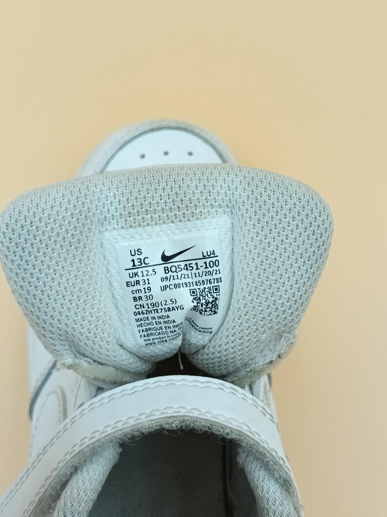 以下が含まれることがあります： 白いベルクロストラップが付いた白い子供用スニーカー。サイズタグには、US 13C、UK 12.5、EUR 31、cm 19、BR 30、CN 190 (2.5)、BQ5451-100、09/11/21/11/20/21、UPC00193145976788、046ZHTE758AYG、インド製、インド製、インド製、インド製、www.nike.comと記載されています。