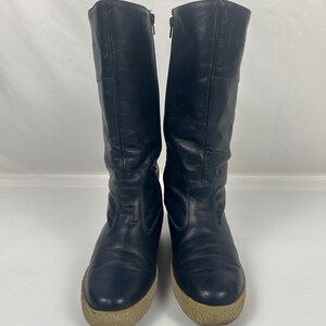 May include: A pair of black leather boots with a zipper closure and a beige sole. The boots are knee-high and have a rounded toe. The boots are in good condition and appear to be vintage.