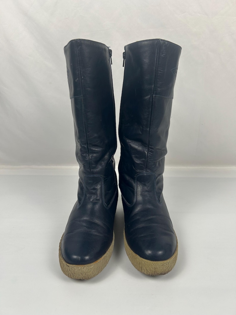 May include: A pair of black leather boots with a zipper closure and a beige sole. The boots are knee-high and have a rounded toe. The boots are in good condition and appear to be vintage.