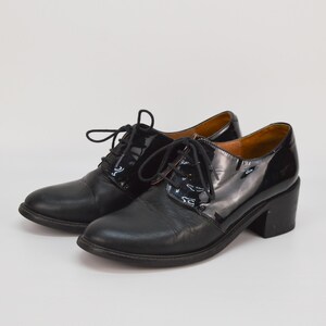 Puede incluir: Zapatos de tac&oacute;n de cuero negro con un panel de charol en el lateral. Los zapatos tienen cierre de cordones.