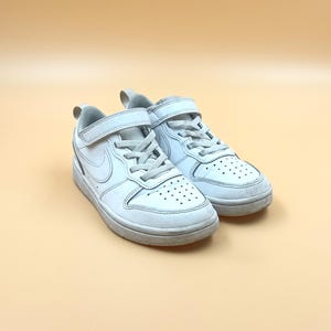 以下が含まれることがあります： 白い革製のベルクロストラップと白いスウッシュロゴが付いたスニーカーのペア