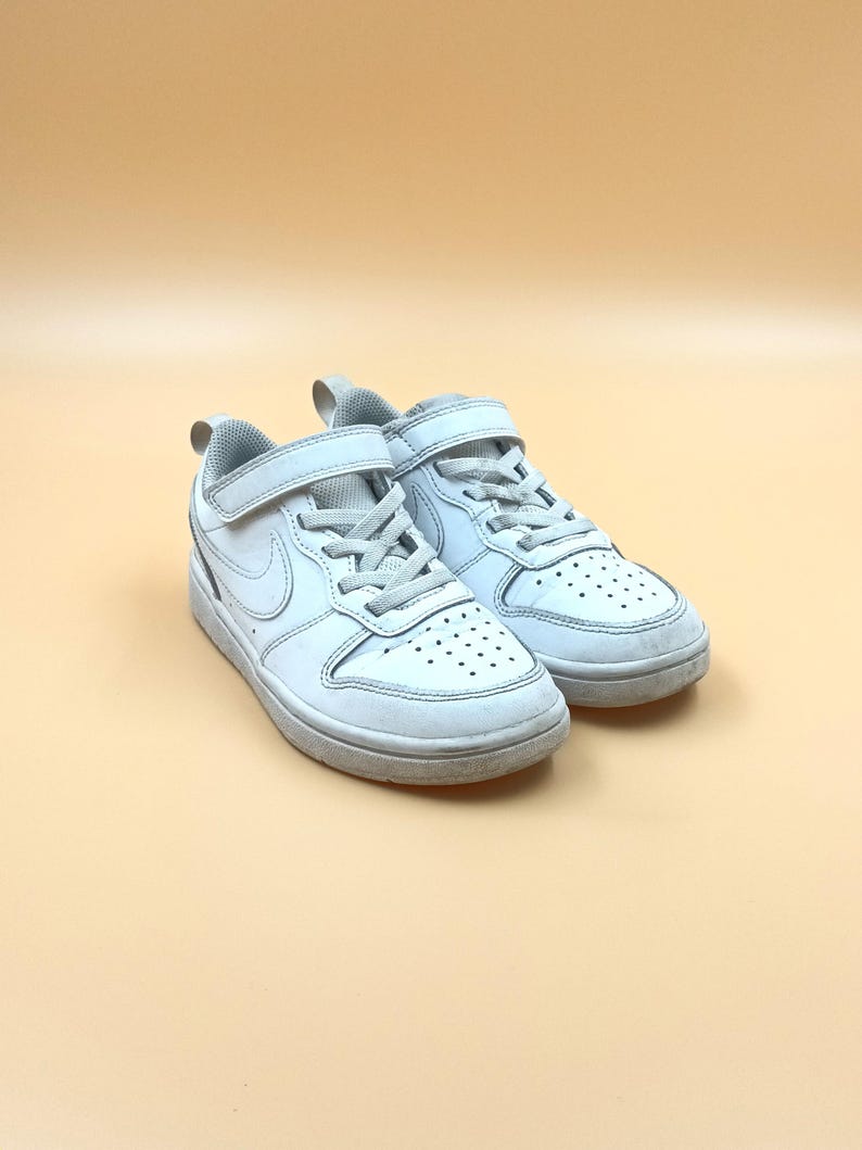 以下が含まれることがあります： 白い革製のベルクロストラップと白いスウッシュロゴが付いたスニーカーのペア