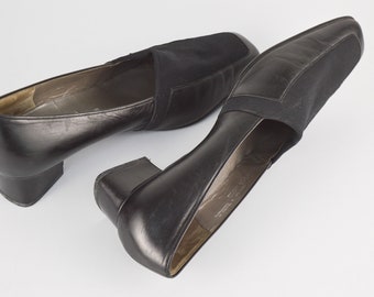 May include: A pair of black leather heeled shoes with a black fabric panel on the top. The shoes have a low block heel.