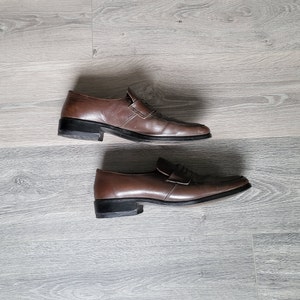 May include: A pair of brown leather loafers with a simple design. The loafers have a black sole and a subtle sheen.