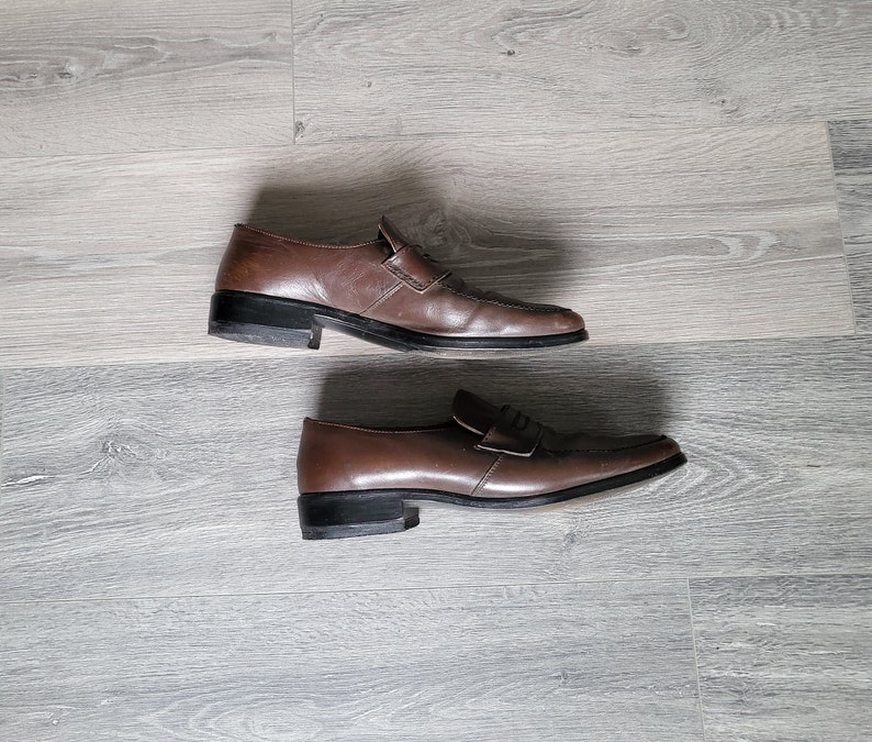 May include: A pair of brown leather loafers with a simple design. The loafers have a black sole and a subtle sheen.