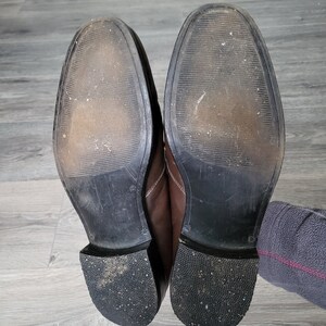 May include: A pair of brown leather shoes with black soles. The shoes are worn and have scuff marks on the soles.