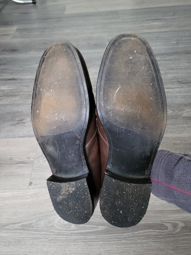 May include: A pair of brown leather shoes with black soles. The shoes are worn and have scuff marks on the soles.