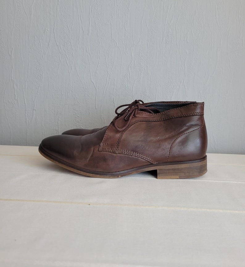 May include: Brown leather ankle boots with laces. The boots have a rounded toe and a low heel.