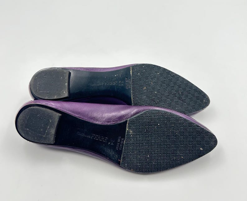 Op de afbeelding: Een paar paarse leren ballerina's met spitse neuzen. De zolen zijn zwart met een textuurpatroon. De schoenen worden op een witte achtergrond gepresenteerd. De merknaam is zichtbaar op de zool.
